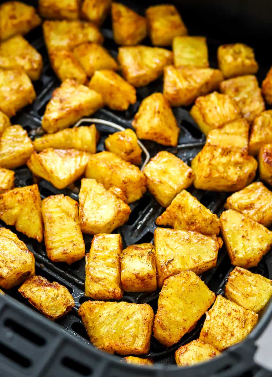 Close-up of cooked glazed pineapple chunks spread out in an air fryer basket.
