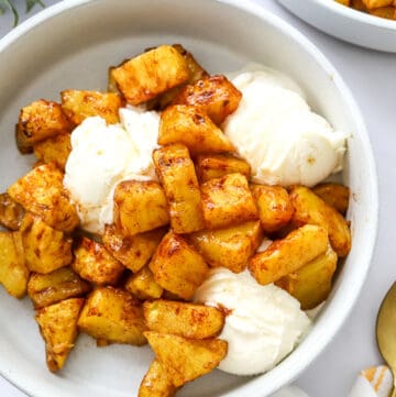 Two bowls filled with golden glazed cinnamon pineapple over vanilla ice cream.