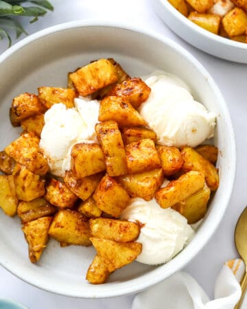 Two bowls filled with golden glazed cinnamon pineapple over vanilla ice cream.