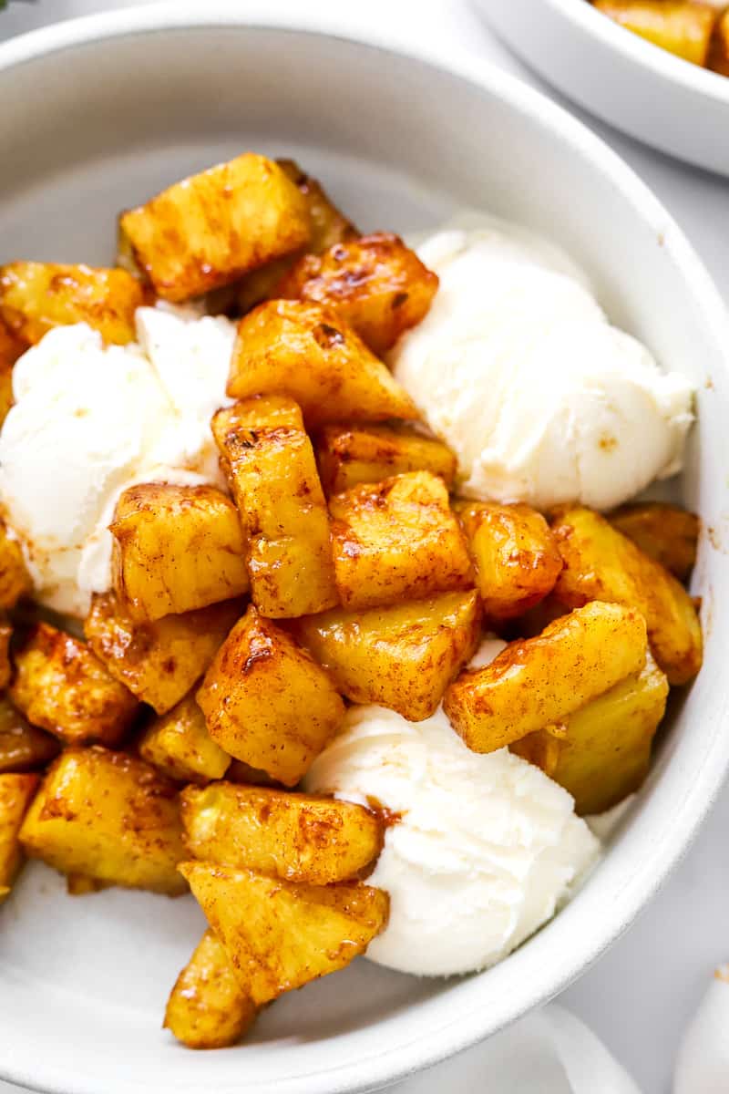 Chunks of cooked cinnamon-glazed pineapple in a bowl with some vanilla ice cream.