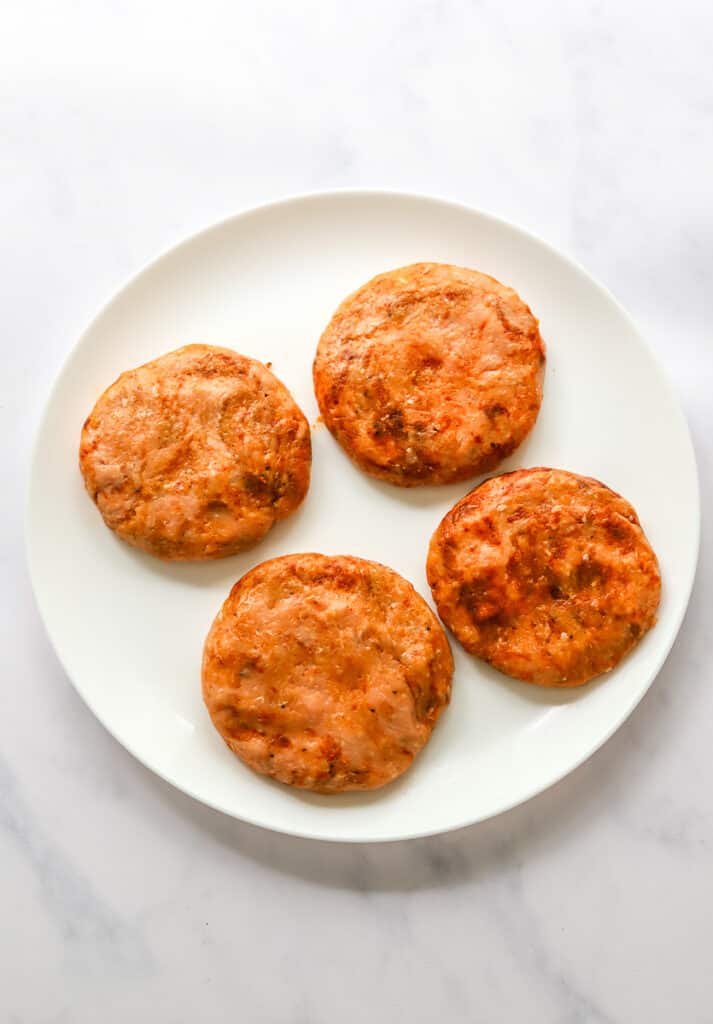 Formed, uncooked, seasoned turkey burgers on a round white plate.