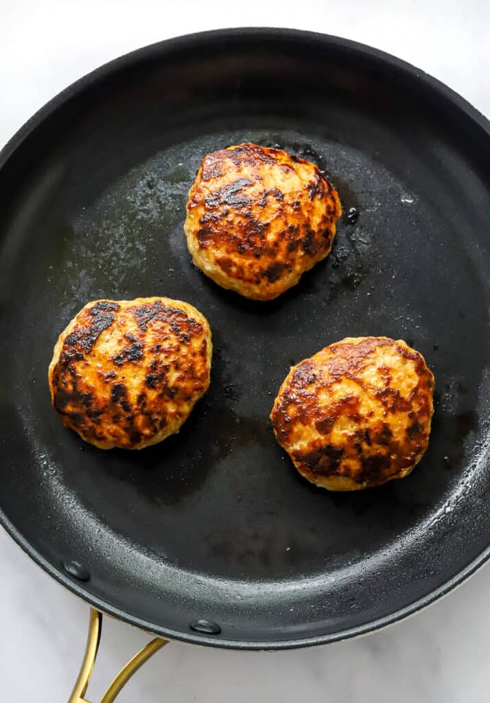 3 turkey burgers cooking in a round black saute pan.