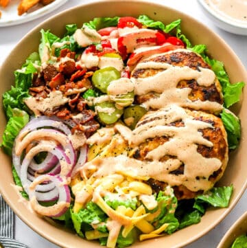 Healthy burger bowl covered in special sauce with a plate of sweet potato fries and a bowl of the sauce behind it.