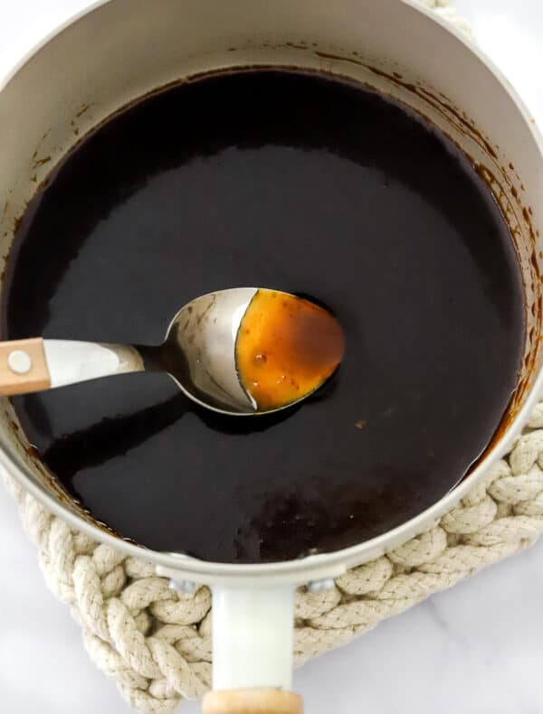 Teriyaki sauce cooking in a white pan with a spoon in the pan with the sauce.