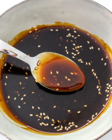 Bowl filled with gluten-free teriyaki sauce topped with sesame seeds in it and a spoon in the center of the bowl of sauce.