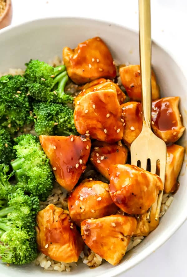 Bowl of chicken teriyaki over rice with steamed broccoli in the bowl next to it.