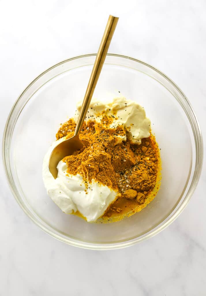 Greek yogurt, curry powder, and mayo in a glass bowl with a gold spoon in the bowl.