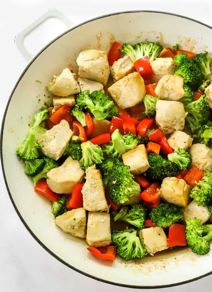 White round skillet filled with cooked cubed chicken breast, broccoli, and chopped bell pepper.