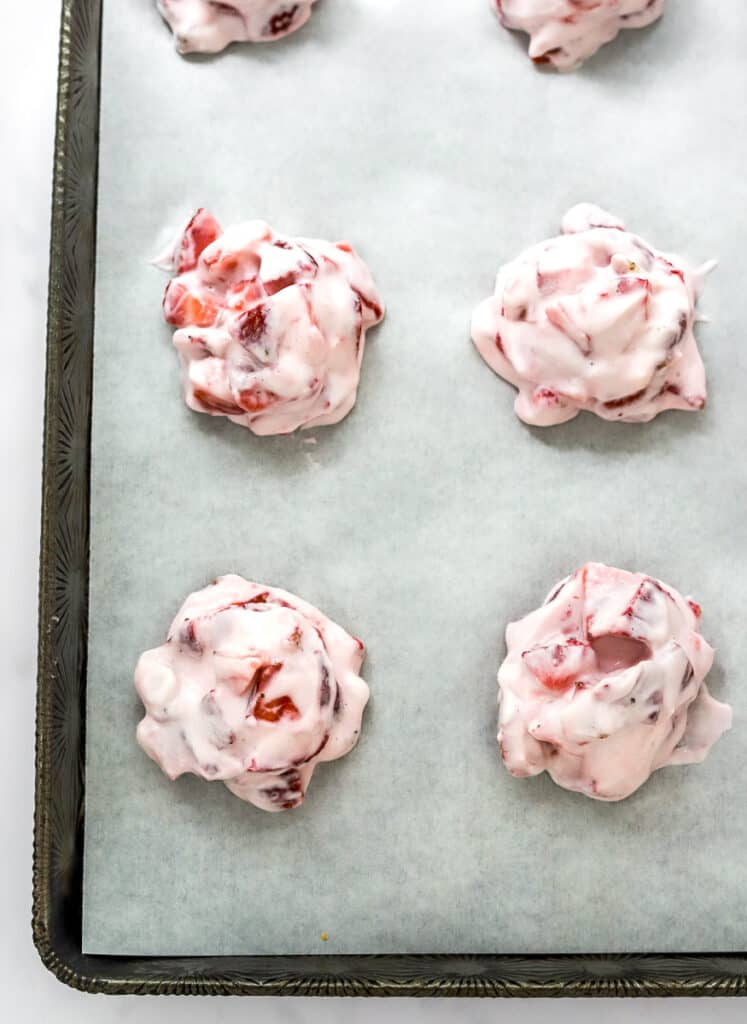 Yogurt strawberry clusters on a baking sheet on top of white parchment paper.