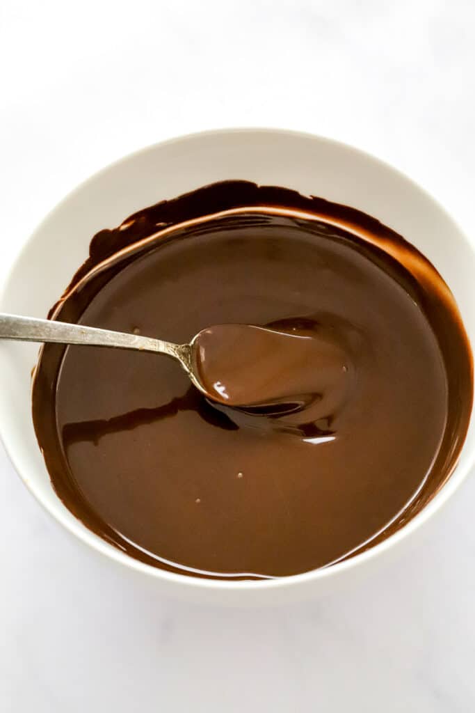 Melted chocolate in a white bowl with a spoon in the bowl.