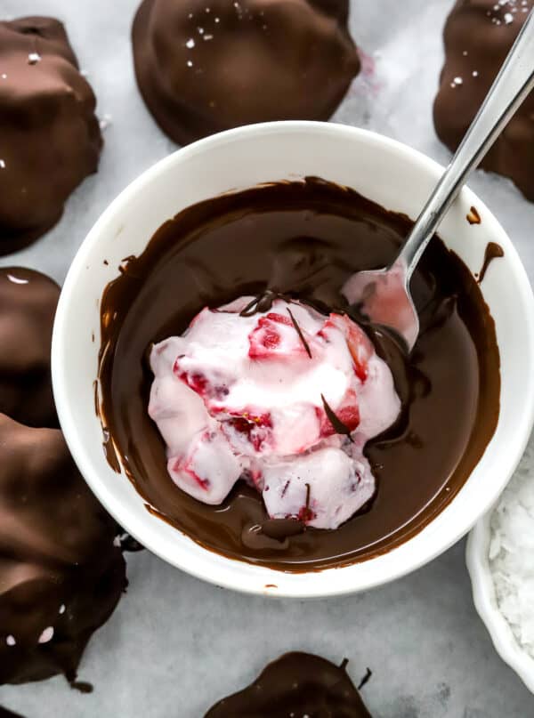 Strawbery yogurt bite being dipped into a bowl of melted chocolate.