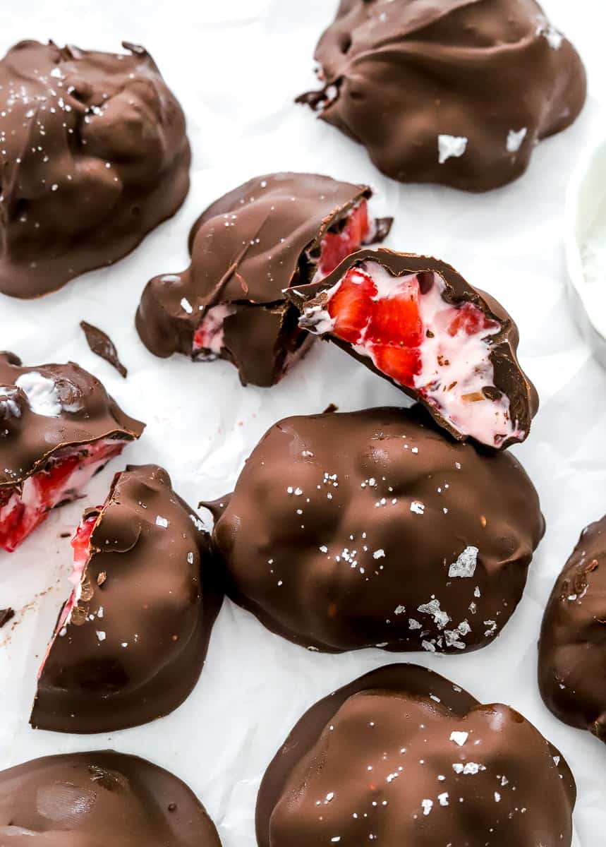A bunch of chocolate strawberry clusters on parchment paper with a few cut open.