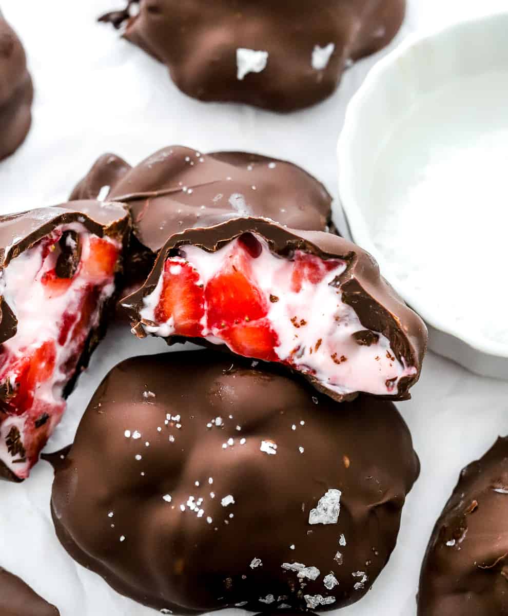 Strawberry chocolate covered yogurt bites cut open on top of another one with more around it.