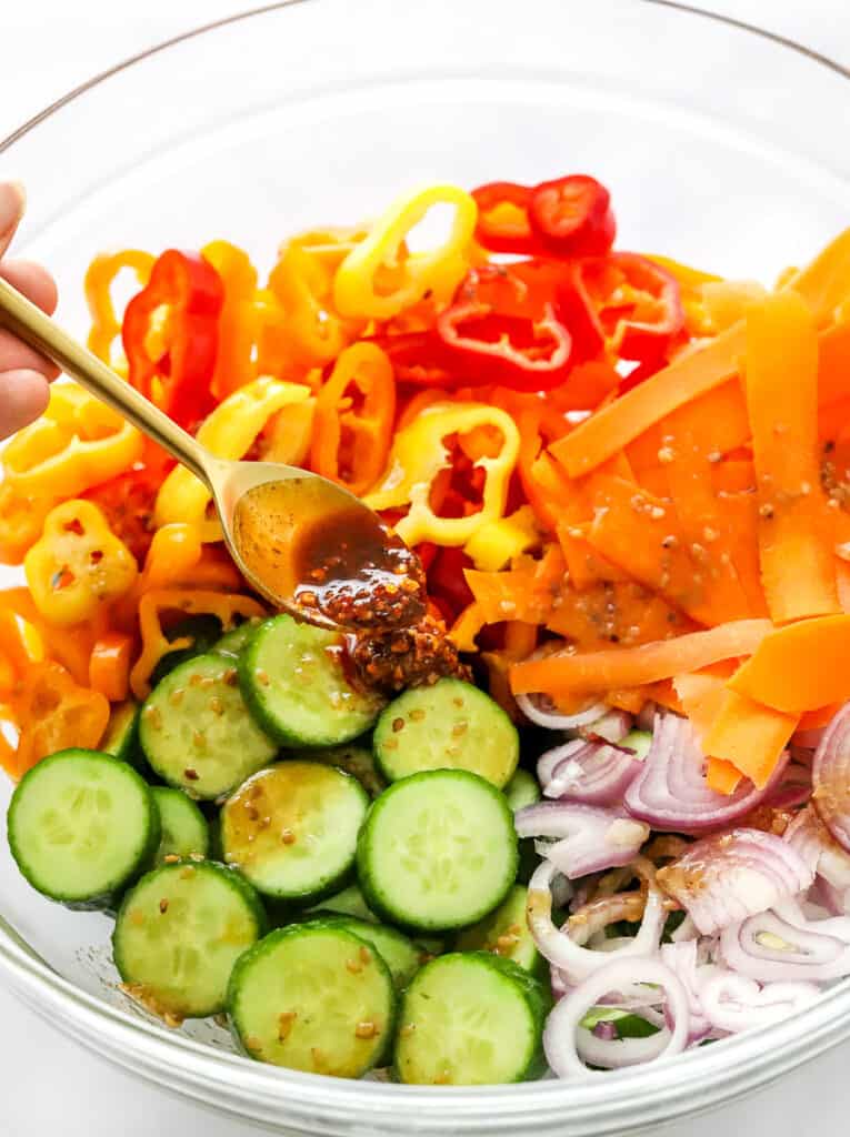 Chilli oil is drizzled onto the cucumbers that are sliced and in a bowl with sliced shallots, chopped peppers and carrot ribbons.