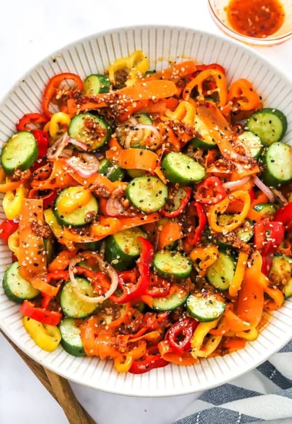 Salad bowl filled cucumber pepper salad with shallots, and carrot ribbons. Mixed with a ginger dressing and topped with bagel seasoning.
