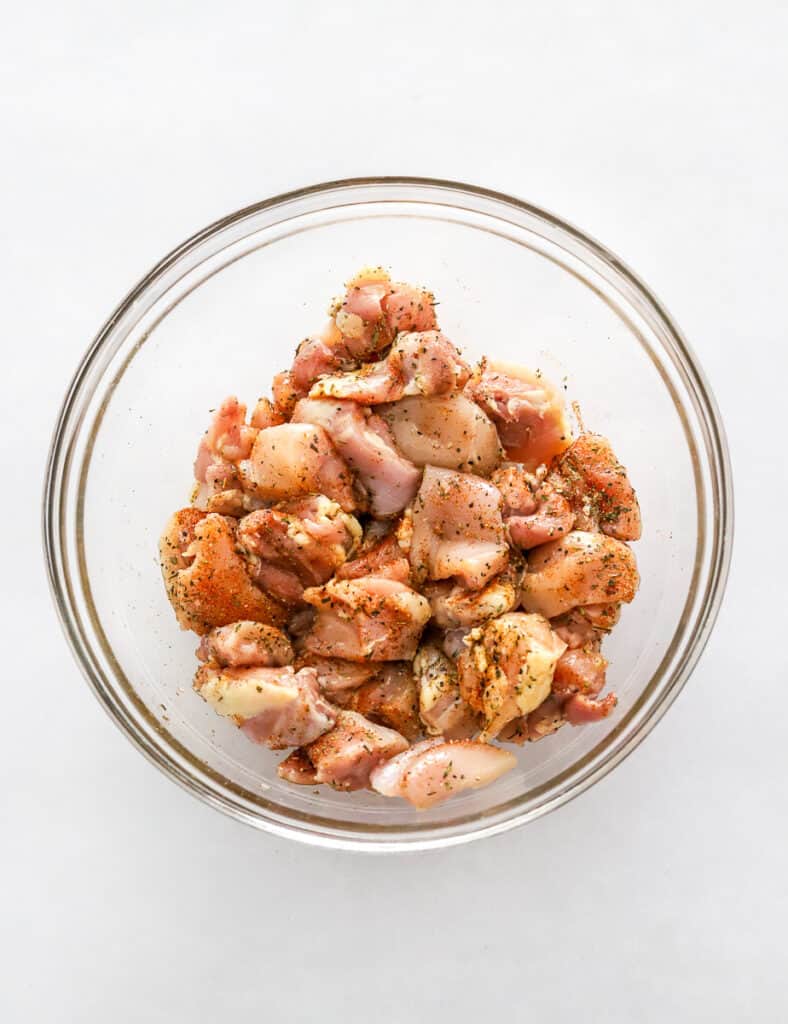 Raw, chopped seasoned chicken thighs in a glass mixing bowl.