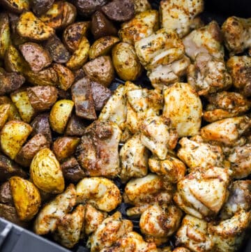 Cooked chopped chicken thighs and cut potatoes in an air fryer basket.