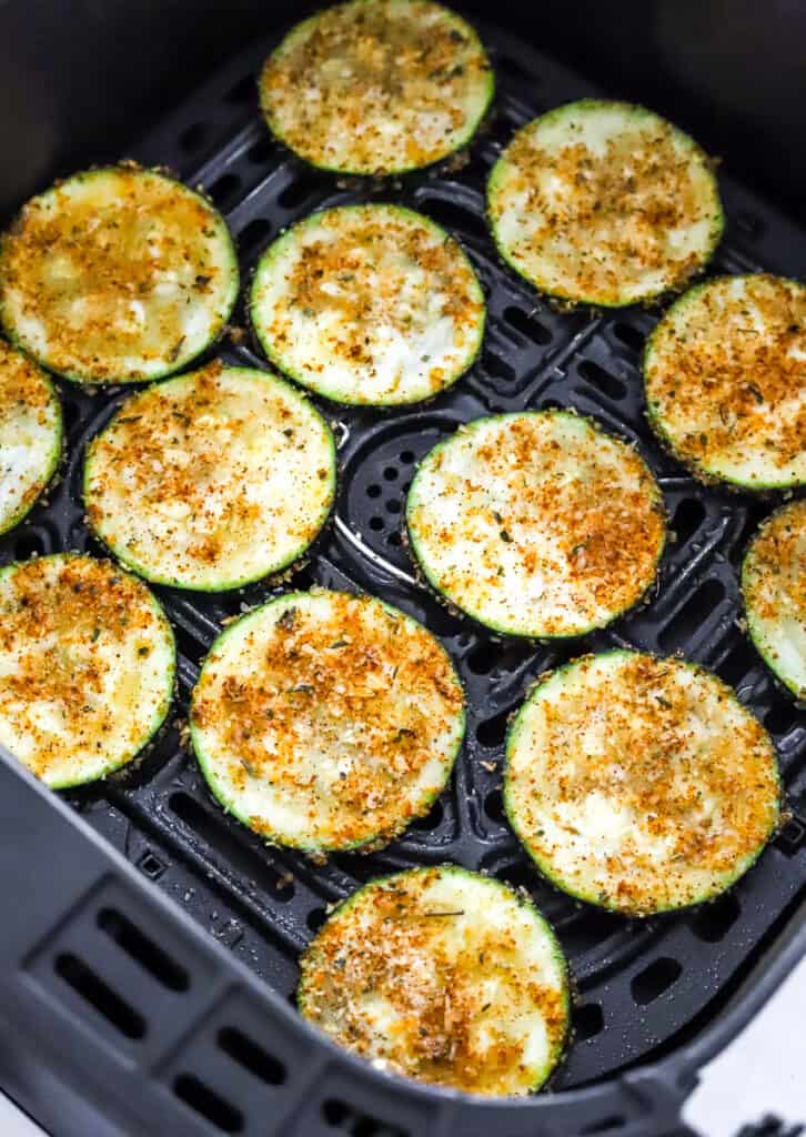 Seasoned uncooked zucchini rounds in an air fryer basket.
