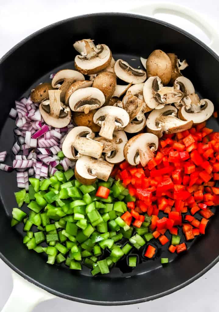 Chopped bell peppers, sliced mushrooms, and diced red onion in a cast iron pan.
