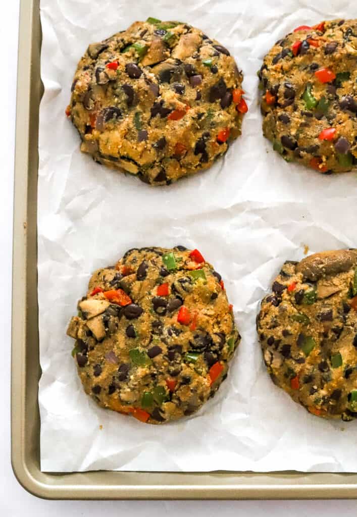 Formed uncooked veggie burgers with black beans in them ontop of white paper on a baking sheet.