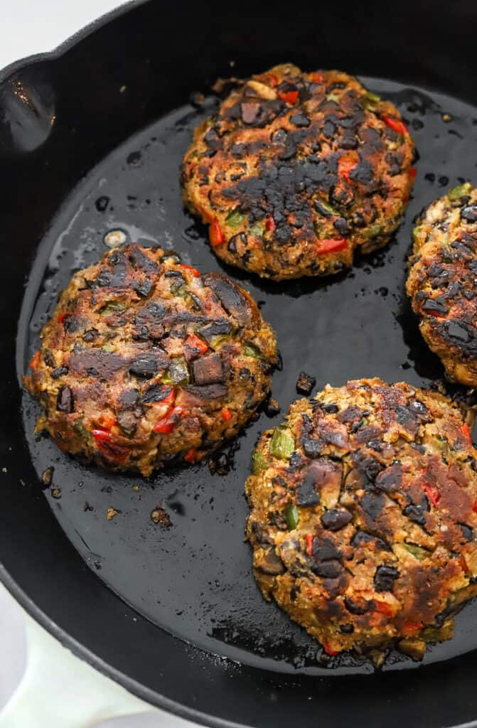 4 black bean burgers cooking in a cast iron pan.