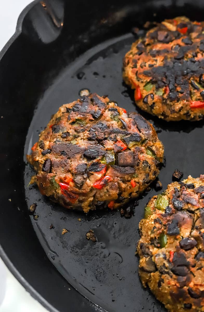 3 burgers made of veggies and beans cooking in a black pan.