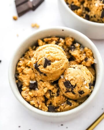 Scoops of cookie dough on too of more cookie dough in a bowl with more behind it.