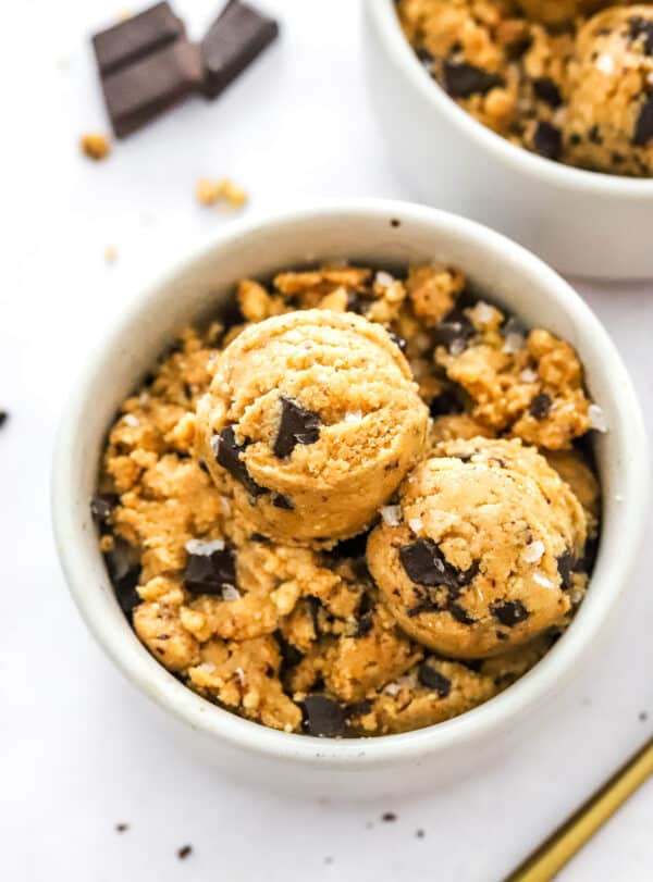 Scoops of cookie dough on too of more cookie dough in a bowl with more behind it.