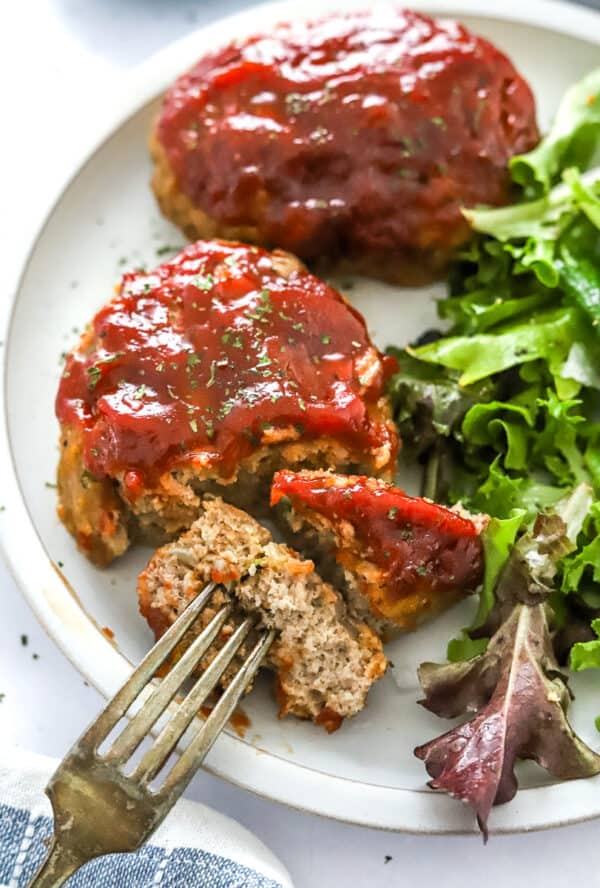 Plate with two mini meatloaf with a side salad on the plate and fork cutting into one of the loaves.