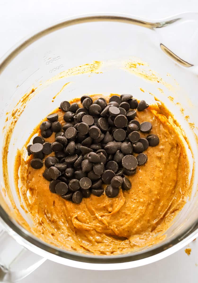 Gass bowl of pumpkin muffin batter with dark chocolate chips in it.