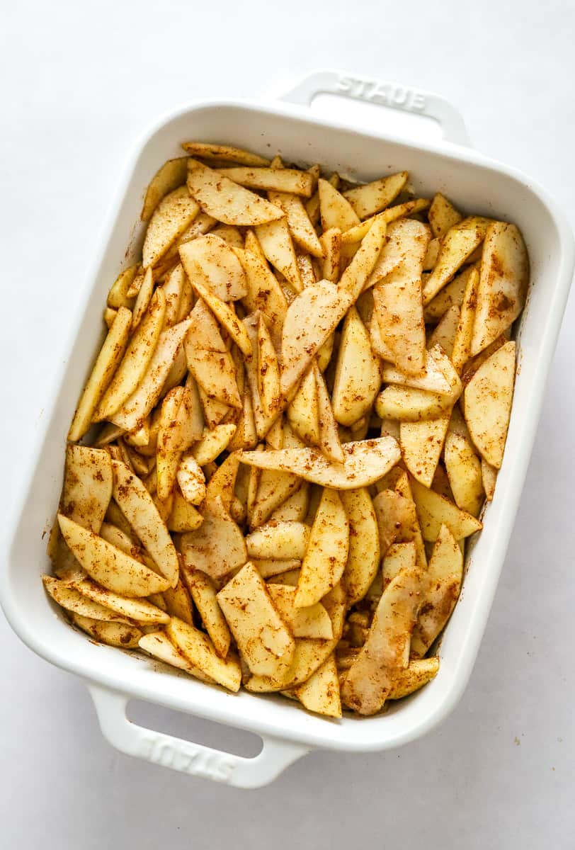 White rectangle pan filled with cinnamon-seasoned sliced uncooked apples and pears.