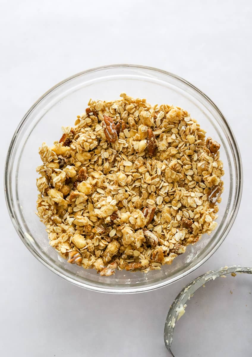 Oat and nut crumble mixed in a round glass bowl with a pastry cutter next to it in front of it.