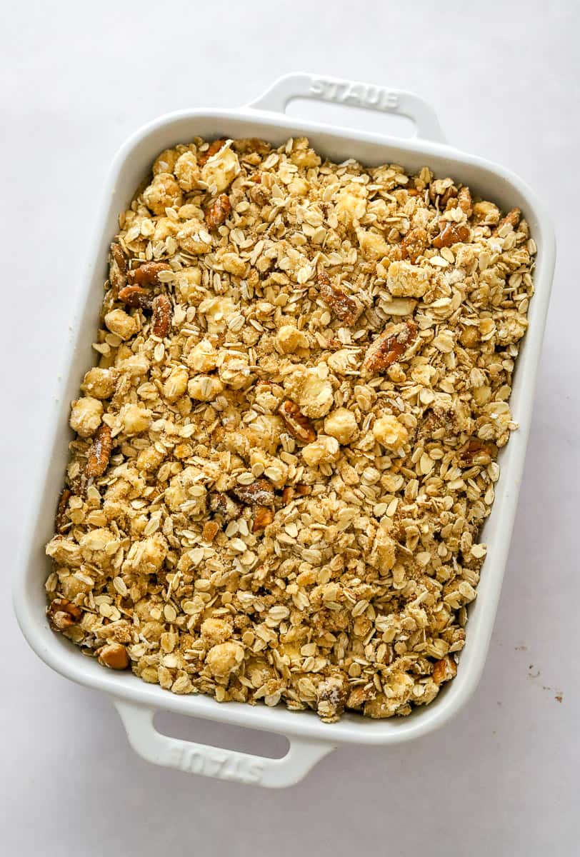 A white baking dish filled with a crumble oat and nut topping before being baked.