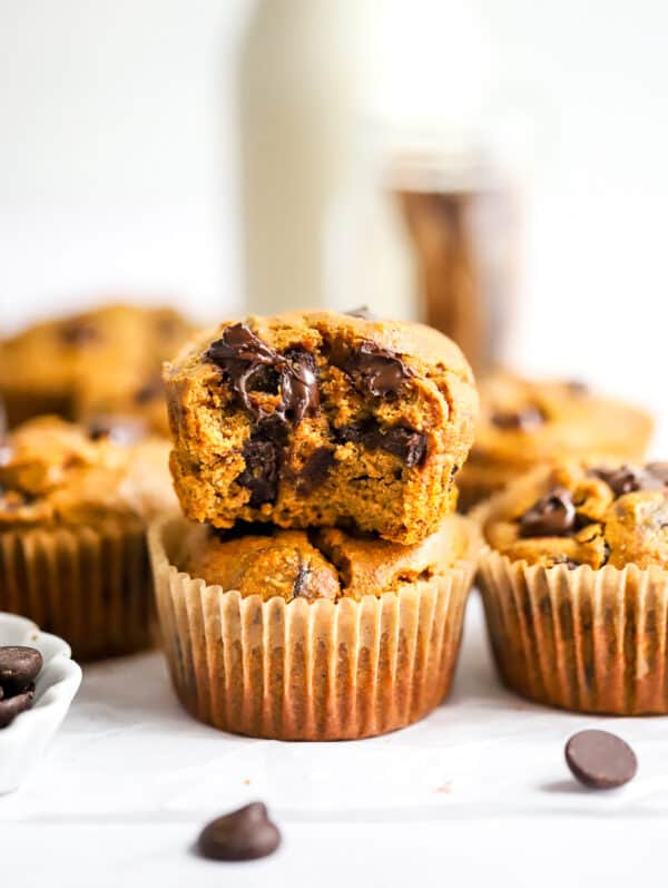 Pumpkin protein muffins with one stacked on top of the other with a bite taken out of it with more muffins behind it.