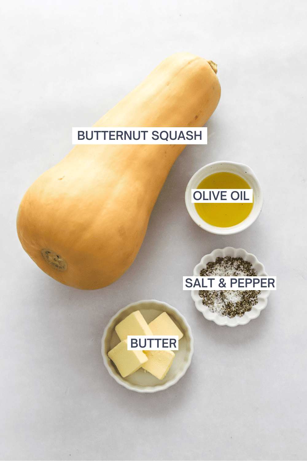 Whole butternut squash with a bowl of olive oil, bowl of salt and pepper and bowl of cubed butter in front of it with labels over each one. 