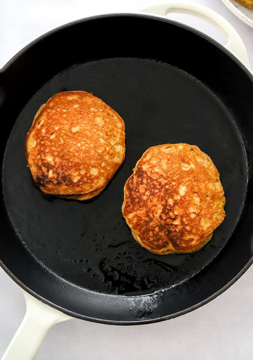 White cast iron pan with two cooked pancakes in it.