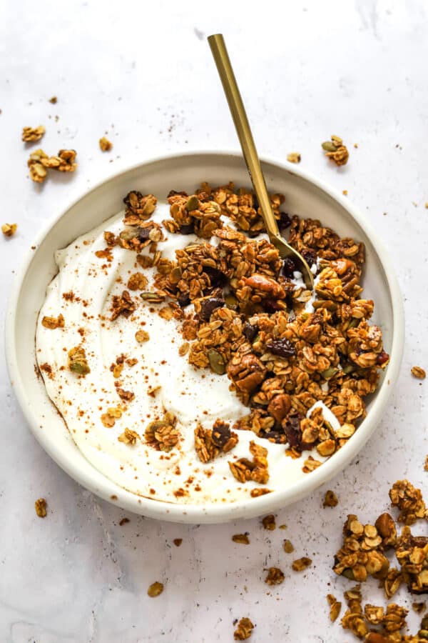 Baked homemade granola on top of yogurt in a bowl with a spoon in the bowl.