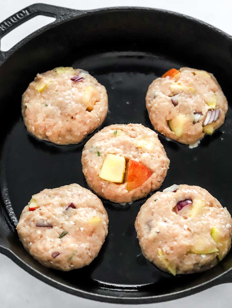 Uncooked chicken apple patties in a cast iron pan.