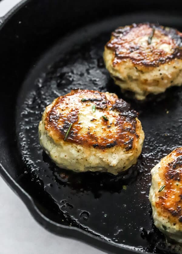 Chicken patties cooking in a cast iron pan.