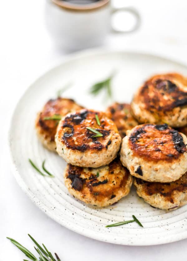 Cooked chicken sausage patties stacked on a plate with herbs in front of it.
