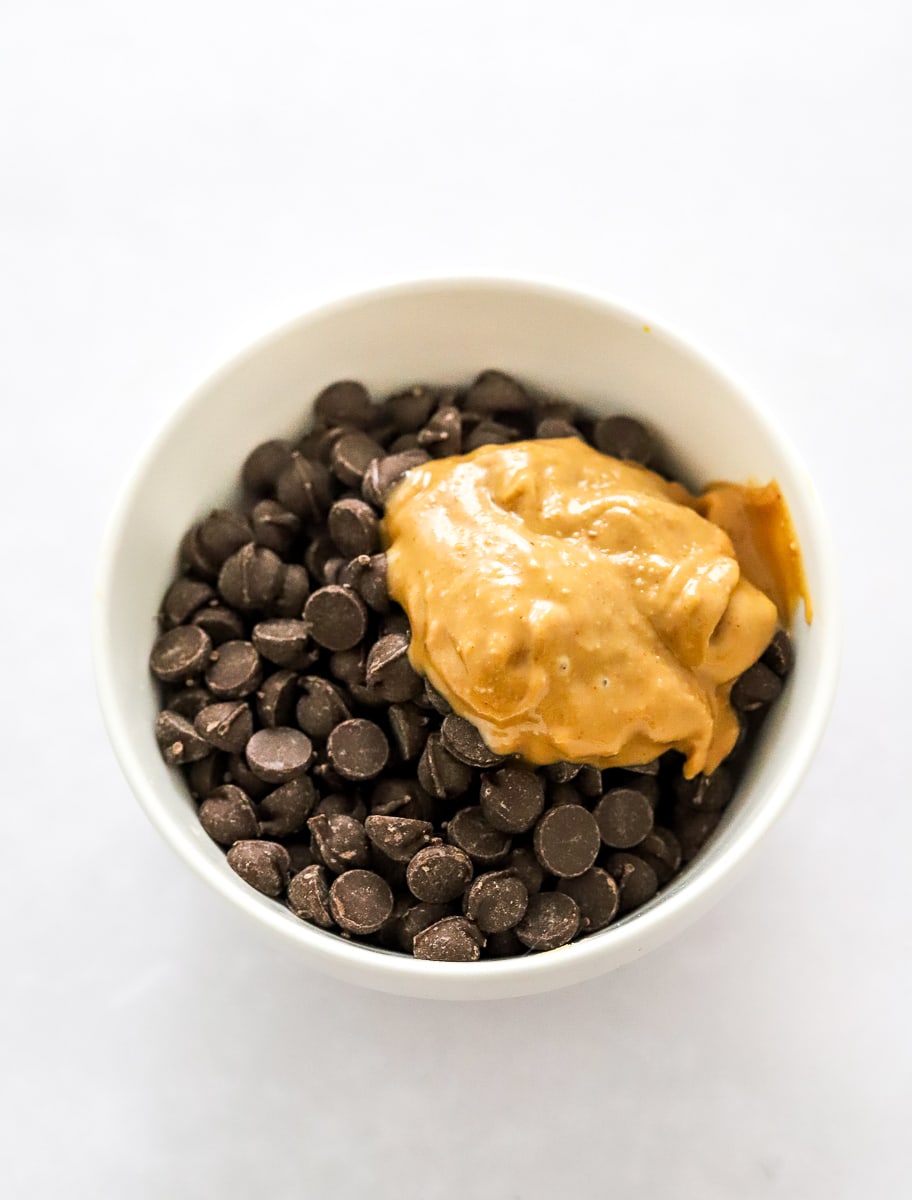 White bowl filled with chocolate chips with a spoonful of creamy peanut butter on top.