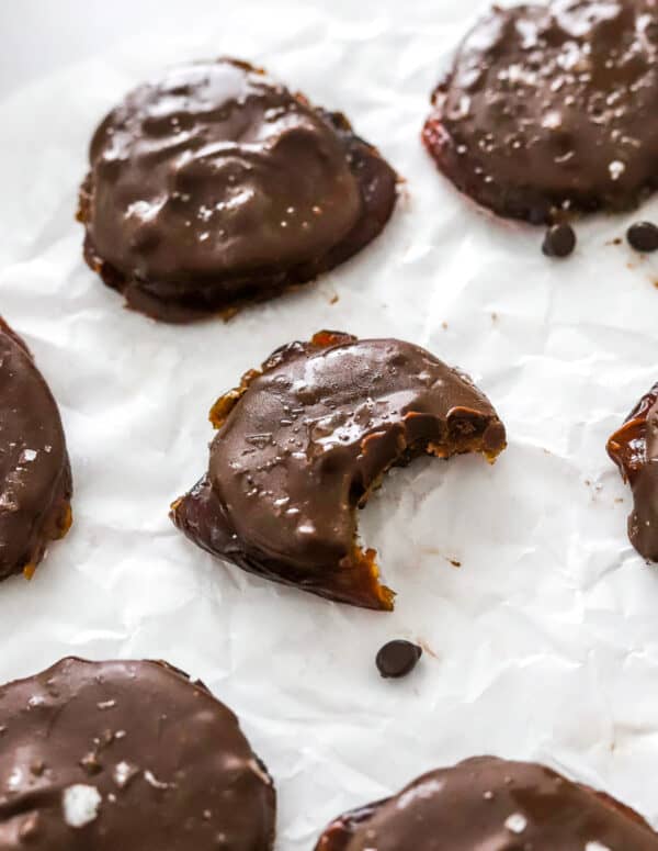 Date cookies covered in chocolate on parchment paper with a bite take out of one of the cookies.