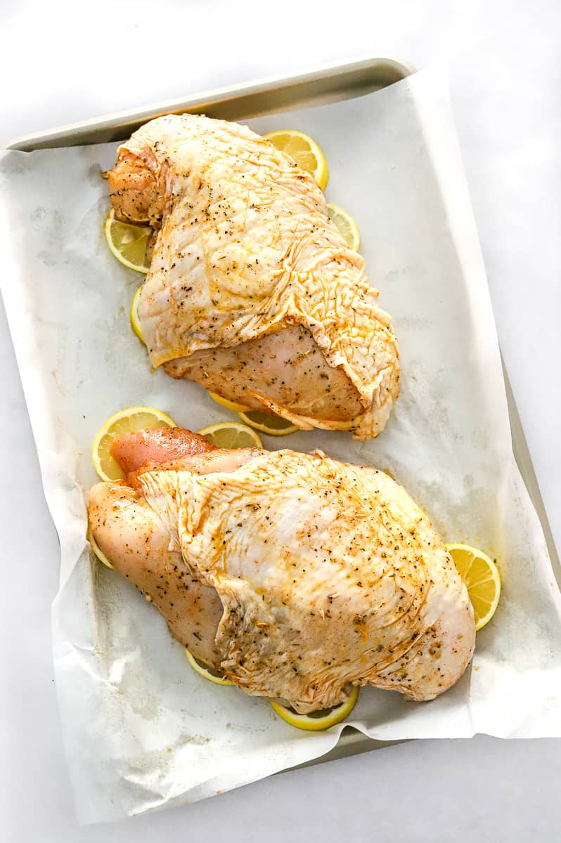 Two boneless turkey breasts seasoned on top of lemon slices on a lined baking sheet.