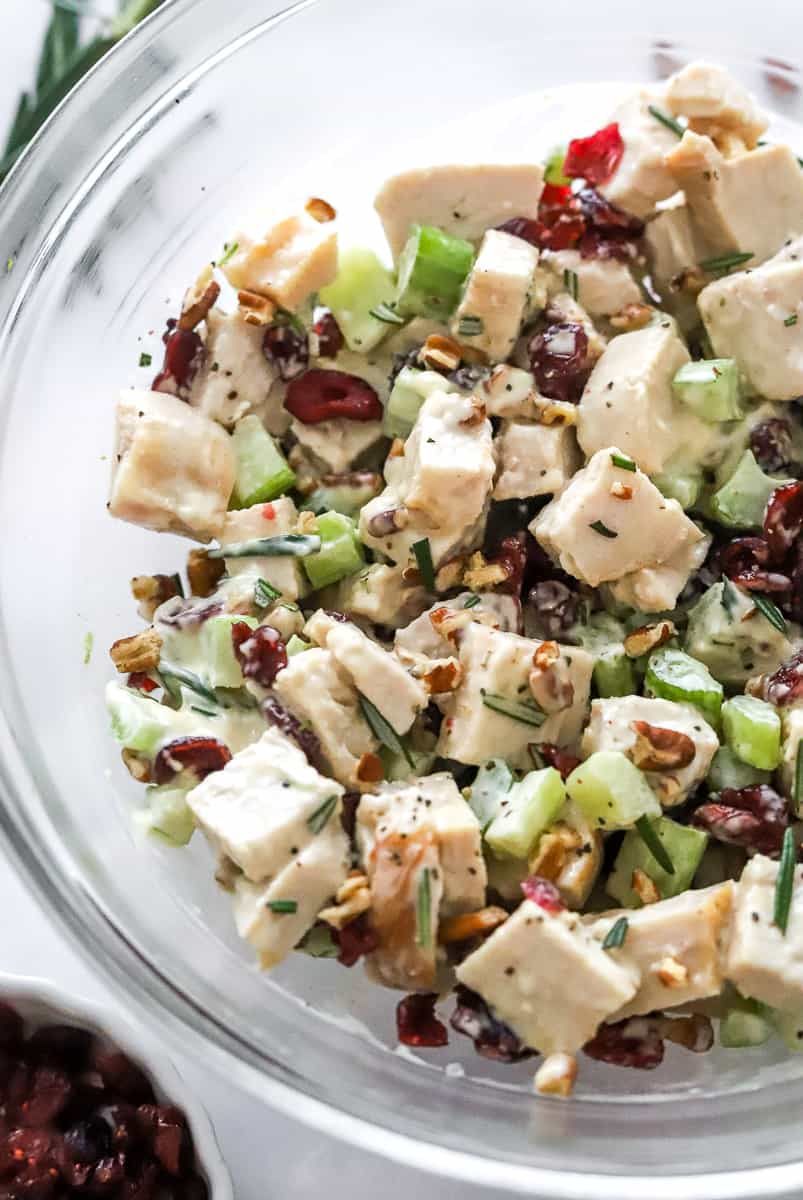 Glass bowl filled with diced turkey salad mixed with mayo, celery, nuts, cranberries and herbs. 
