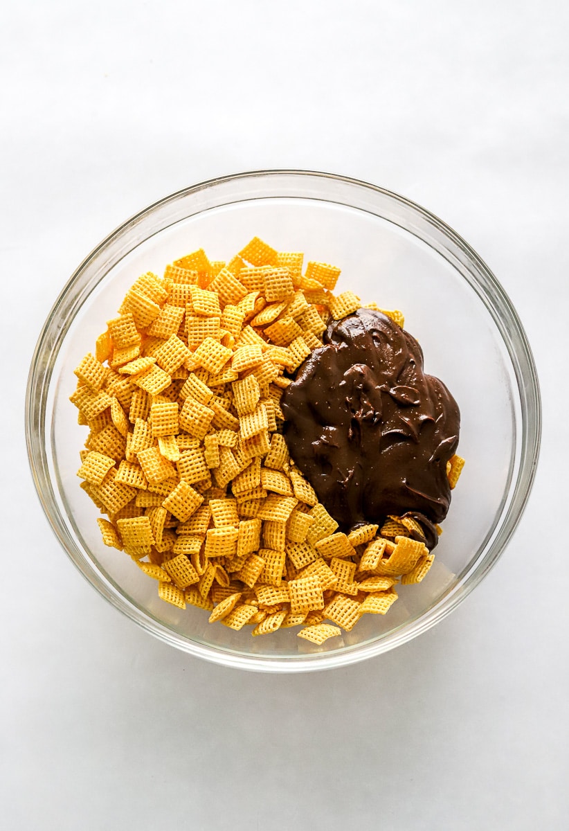 Honey nut Chex cereal with melted chocolate next to it in a round, glass mixing bowl.