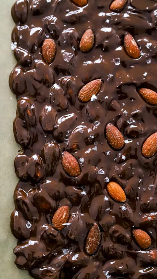 Side shot of melted dark chocolate tossed with almonds spread out on a baking sheet.