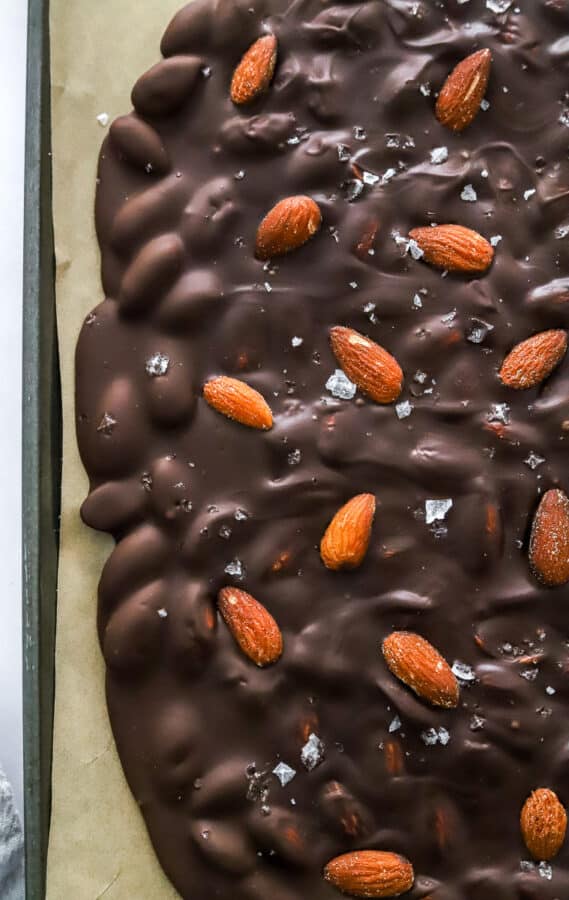Side shot of chocolate bark with almonds on a lined baking sheet.