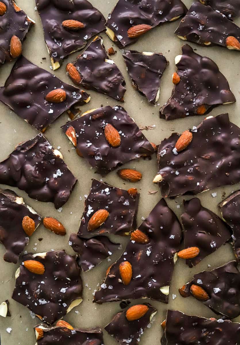 Several pieces of chocolate bark topped with almonds broken into large pieces on to ob brown parchment paper.