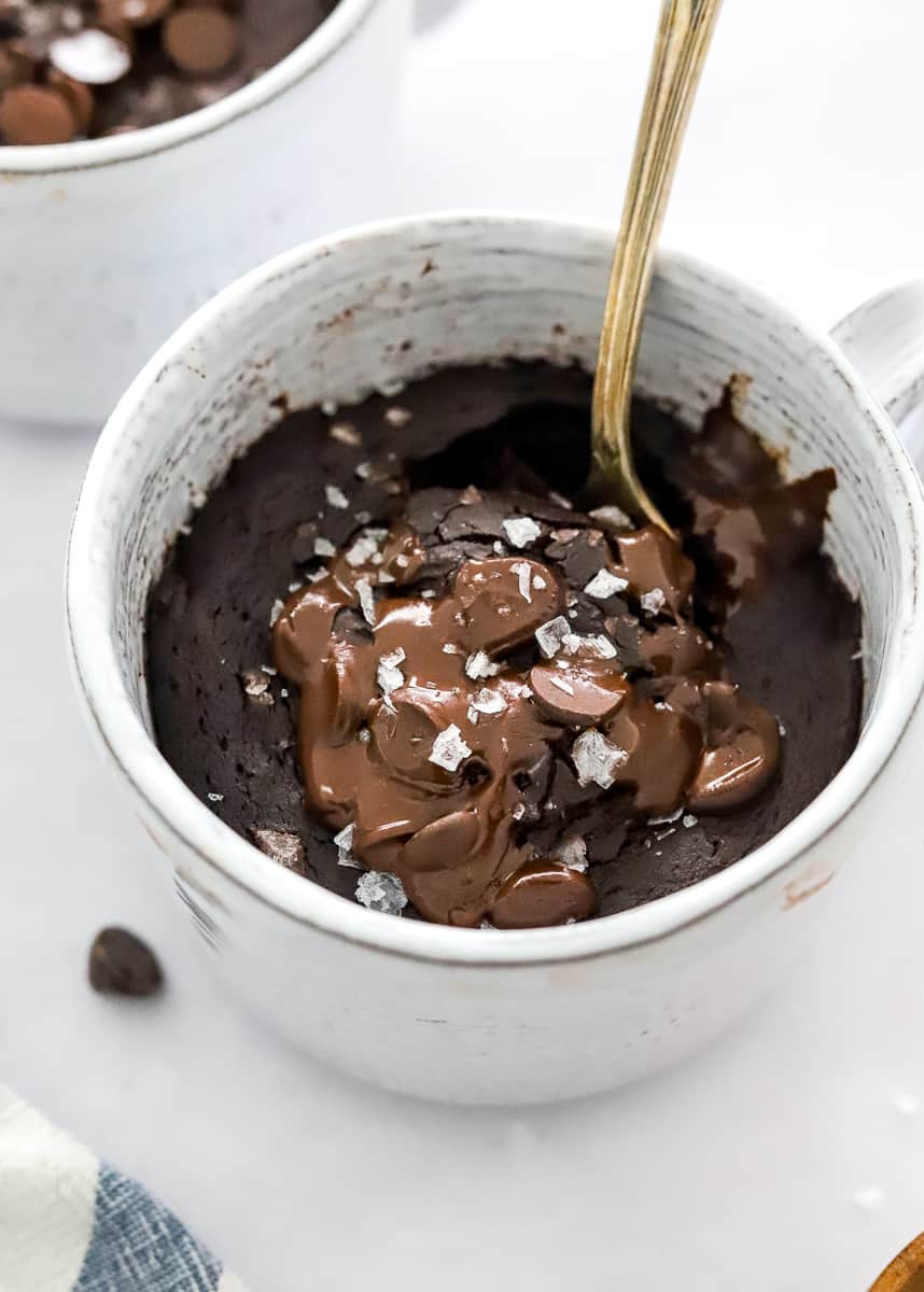 Chocolate protein mug cake topped with chocolate and sea salt with a spoon in the dish.