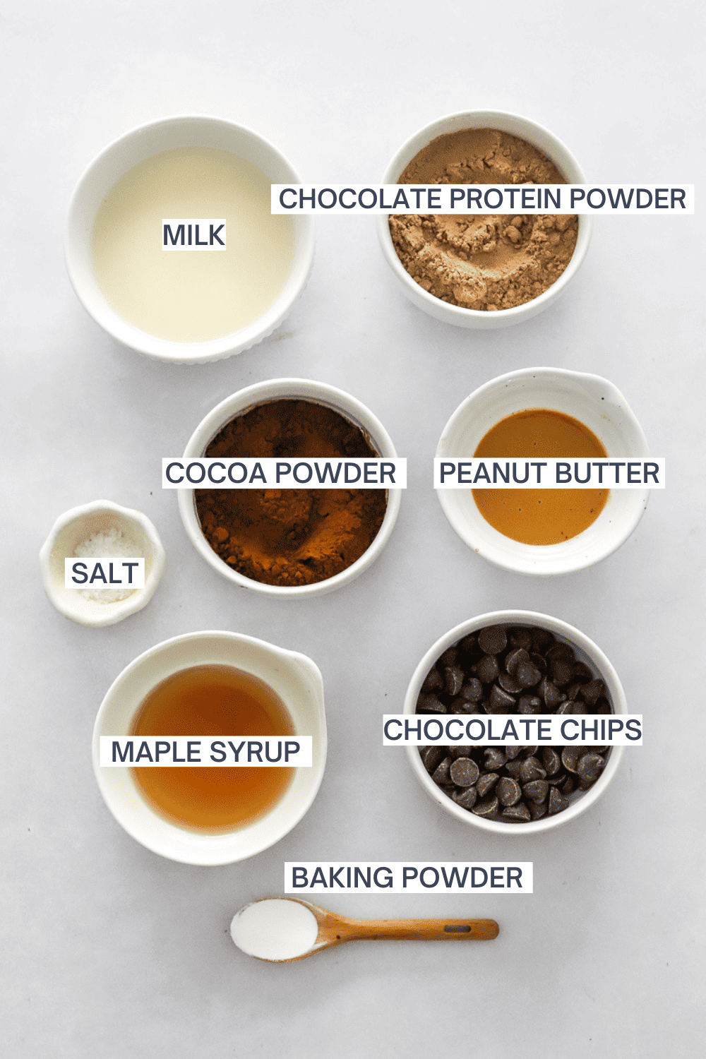 Ingredients for a chocolate protein mug cake in bowls with labels over each ingredient.